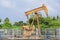 Old rusty isolated oil pump jack extracting crude oil and natural gas from well in green and cloudy oil field