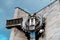 Old, rusty, metal timepiece in form of owl on building. Vintage, big, electronic clock on street in cloudy weather.