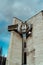 Old, rusty, metal timepiece in form of owl on building. Vintage, big, electronic clock on street in cloudy weather.