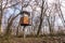 An old, rusty, military watchtower located in the woods. Early spring, trees without leaves and metal observation tower