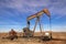 Old rusty oil well pump jack sitting in field with bright blue dramatic sky - head of machinery looks like a funny face