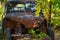 An old rusty retro car stands on a street on a summer day under green trees. An old retro car