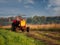 Old rusty tractor with grass cutting machine in a agriculture field with tall grass at stunning sunrise. Farming industry.