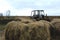 Old rusty tractor and hay bales under a cloudless sky. Dry hay in the foreground and a bright sky