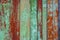 Old rusty wood wall from row of planks, painted green with spots of first red wood layer