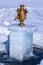 An old samovar stands on a piece of melted ice on a blurry snow background.