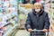 Old senior european man wearing protective facial mask pushing shopping cart in the supermarket. Shopping during COVID-19 concept