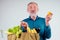 Old senior grandfather holding cotton reusable shopper bag full of natural farmer vegetables:corn,bananas grapes