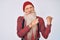 Old senior man with grey hair and long beard wearing hipster look with wool cap pointing to the back behind with hand and thumbs