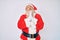 Old senior man with grey hair and long beard wearing santa claus costume with suspenders begging and praying with hands together