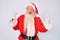 Old senior man with grey hair and long beard wearing santa claus costume with suspenders shouting with crazy expression doing rock