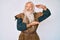 Old senior man with grey hair and long beard wearing viking traditional costume gesturing with hands showing big and large size