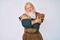 Old senior man with grey hair and long beard wearing viking traditional costume hugging oneself happy and positive, smiling