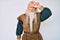 Old senior man with grey hair and long beard wearing viking traditional costume making fun of people with fingers on forehead