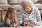 Old senior woman teaching small granddaughter coloring images.