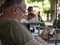 Old sernior white man sitting in a cafe looking at an Apple IPhone 4 smartphone using the mobile internet data.