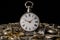 Old silver pocket watch on a pile of gears, gearwheels, cogwheels and metal bracelet on black isolated background