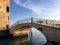 An old small historic stone bridge with iron railings crossing a canal with the open ocean in the background in Northern Venice