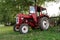 Old small red agriculture tractor parked on the grass summertime before sunset three-quarter view