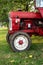 Old small red agriculture tractor parked on the grass summertime before sunset three-quarter view