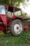 Old small red agriculture tractor parked on the grass summertime before sunset three-quarter view