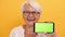 Old smiling woman showing the smartphone. Green screen for replacement