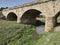 Old soviet bridge made of stone. Little gray river. Green grass