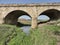 Old Soviet bridge made of stone. A small stream in the middle of green grass and flowers. Blue sky