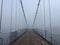 Old spooky suspension bridge foggy entrance. Altai village bridge. Early misty morning