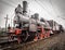 Old steam engine locomotive with puffs of white steam passes a turn on the railroad