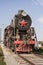 An old steam locomotive with red wheels and a red star stands in an open-air Museum on the seaside Boulevard embankment in Baku, A