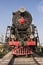 An old steam locomotive with red wheels and a red star stands in an open-air Museum on the seaside Boulevard embankment in Baku, A