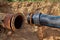 An old steel water pipe with a welded flange lies next to a new plastic pipe