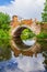 Old stone bridge arch with reflection in water, ruined historic architecture
