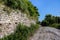 An old stone-paved road that passes past an ancient stone wall covered with greenery.