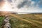 Old stone wall and small country road. West coast of Ireland. Atlantic ocean, Beautiful cloudy sky. Sun flare. Nobody. Irish