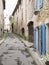 Old street with lonely figure and house with shutters and plants in manosque