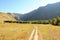 An old striped field road traverses a field at the bottom of a deep canyon surrounded by high mountains