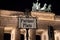 An old style signpost with the German name Pariser Platz Paris Square which is placed in front of the illuminated Brandenburger