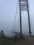 Old suspension bridge fog view. Altai village bridge. Early misty morning