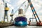 An old tanker moored in a dockyard surrounded by large lifting cranes