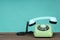 Old telephone on wooden table in front of green background. Vintage phone with taken off receiver. Vintage style photo