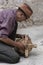 Old Tibetan man repairing ancient wooden prayer wheel