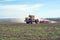 An old tractor is dragging a modern aggregate for tillage leveling the field surface