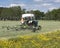 Old tractor and hay tedder in meadow near field full of buttercups