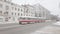 An old tram with passengers passes through the city street on a snowy winter day