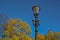 Old vintage black decorative lantern with glass lamps on pillar, pole in bright yellow spring forest. Blue sky. Saint Petersburg c