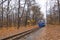 Old vintage blue railway train on the track rails front view. Railroad single track through the woods in autumn. Fall landscape