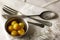 OLD VINTAGE CUTLERY ARRANGED ON A WHITE NAPKIN WITH YELLOW GOOSEBERRIES IN A METAL BOWL