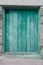 Old vintage low green door. Entrance from wooden panels and boards with shabby emerald paint. Hole for cats on top. The house is